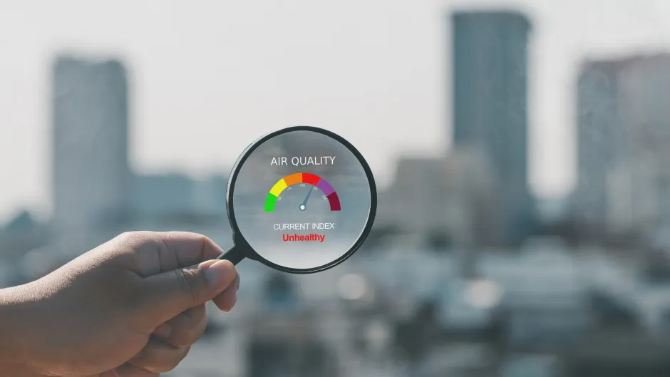 Lupe mit "Messeinrichtung" für Luftqualität vor unscharfer Stadtsilhouette